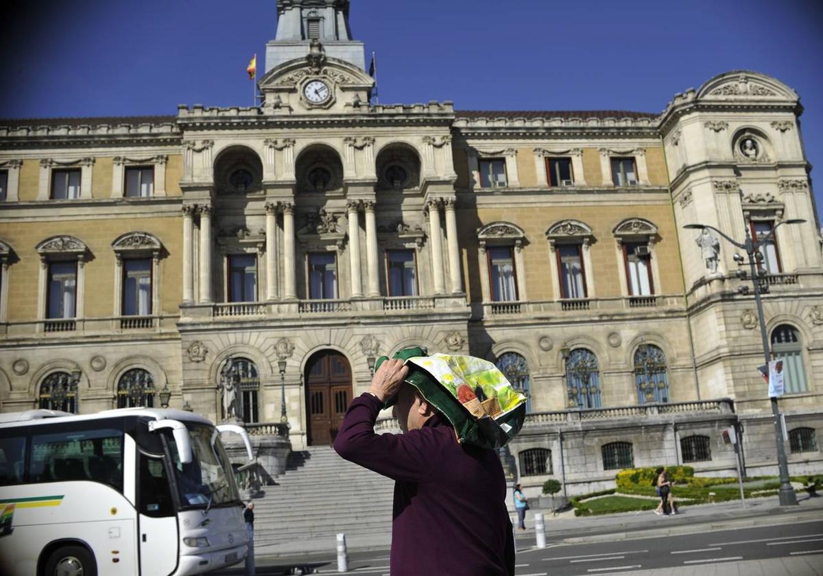 Un hombre se protege del sol ante el Ayuntamiento.