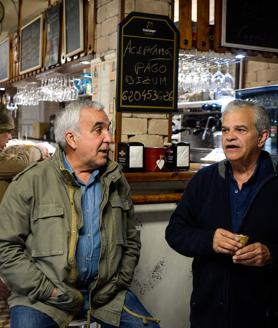 Imagen secundaria 2 - Raúl recostado en una casa de Lanestosa. Otra vecina de la villa, Pili Ranero, pasa con un bizcocho junto al panel de anuncios. José Ángel y Manuel conversan en el Bar Rosi.