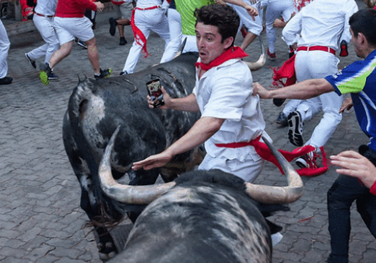 Un corredor se zafa entre dos toros con la cámara del móvil encendida en el encierro de este domingo en San Fermín.