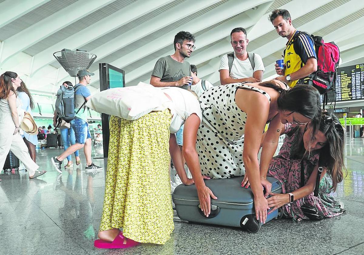 Tres chicas se afanan en cerrar la maleta junto a los mostradores de embarque del aeropuerto de Loiu.