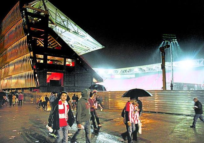 Aficionados se refugian de la lluvia mientras contemplan el estado inacabado del nuevo San Mamés.