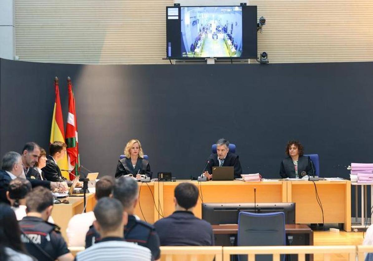 El tribunal de la Audiencia de Gipuzkoa y, a su derecha, el fiscal y varias de las defensas. De espaldas, en el primer banco custodiados por ertzainas, tres de los procesados.