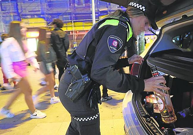 Una policía local guarda una botella incautada a un menor.