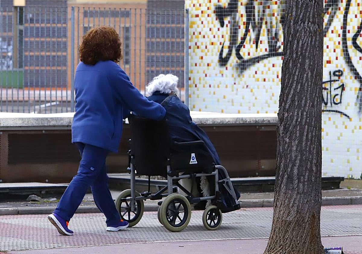 Una mujer pasea a una anciana en silla de ruedas.