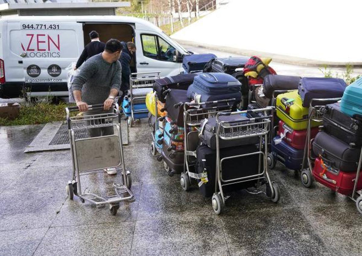 Imagen secundaria 1 - Arriba, largas colas en el 'hall' de salidas de Loiu. A la izquierda, empleados de una empresa de transporte cargan en furgonetas las maletas que se han quedado en tierra. A la derecha, usuarios reciben información de parte de una trabajadora con las cintas transportadoras colapsadas.