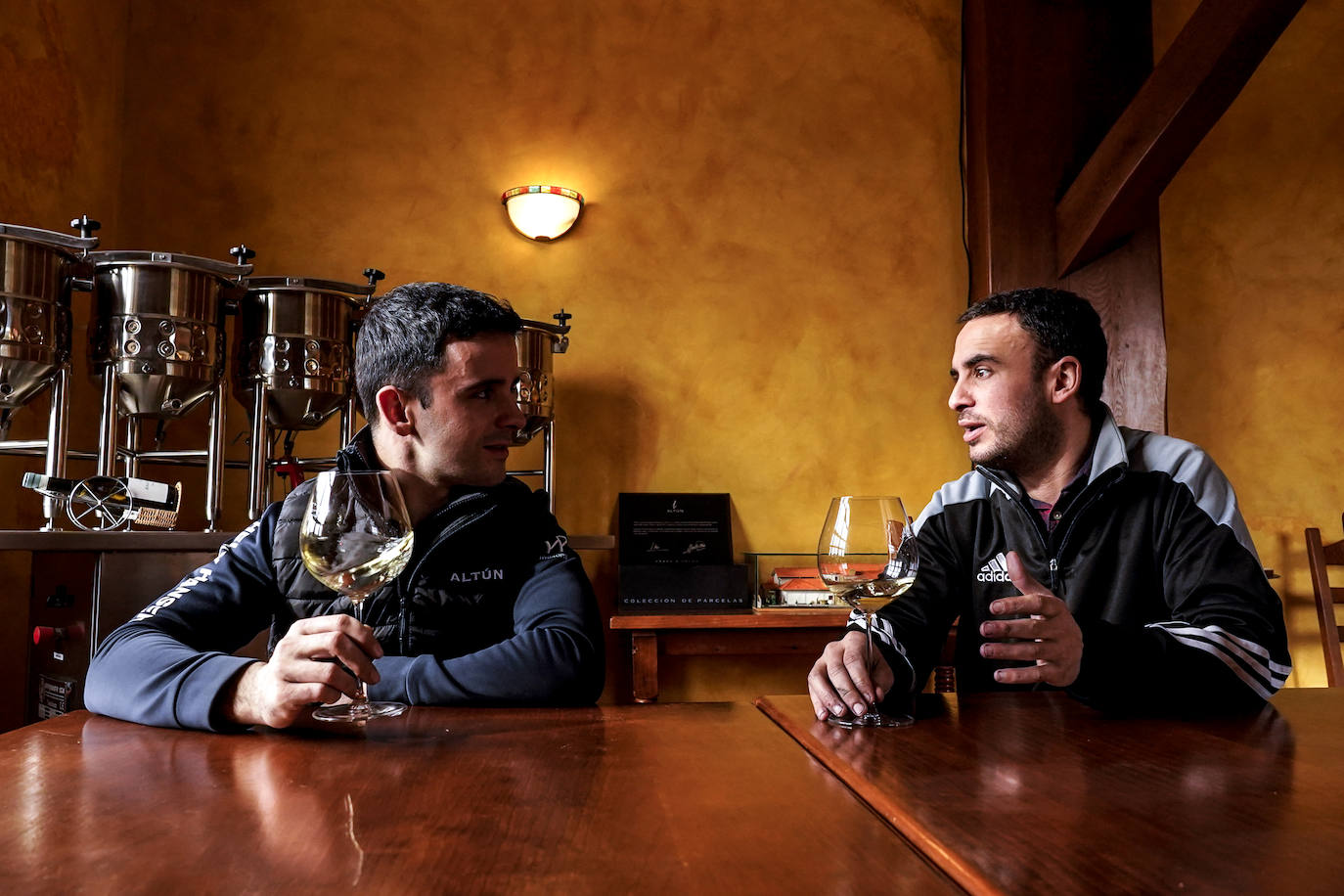 Los hermanos Martínez Pangua charlan en la bodega con una copa de su vino blanco.