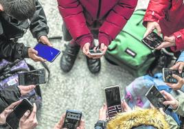 Varios adolescentes con sus teléfonos móviles en corro a la salida de un centro educativo.