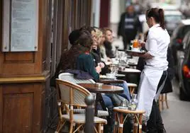 Una camarera lleva su consumición a los clientes de una terraza.