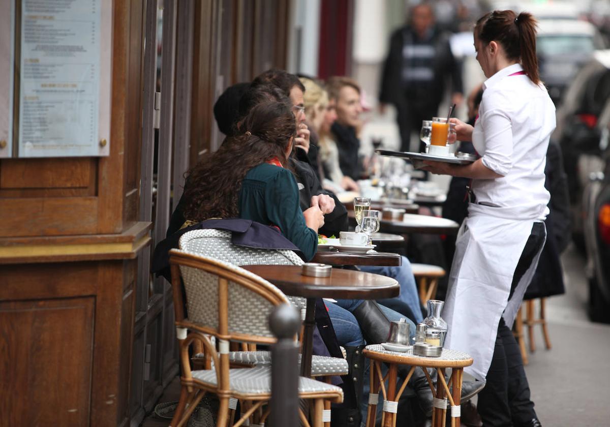 Una camarera lleva su consumición a los clientes de una terraza.