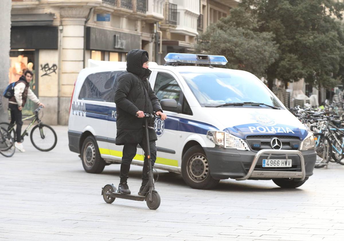 Un joven ajeno a la información pasa con su patinete frente a una furgoneta de la Policía Local de Vitoria.