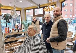 Jesús Peña, en primer término, junto a su padre, Dionisio, y Josu Gómez, uno de sus empleados, atendiendo a dos clientes habituales de la barbería.