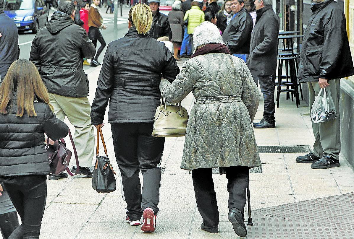 Una persona mayor camina abrazada a su cuidadora.