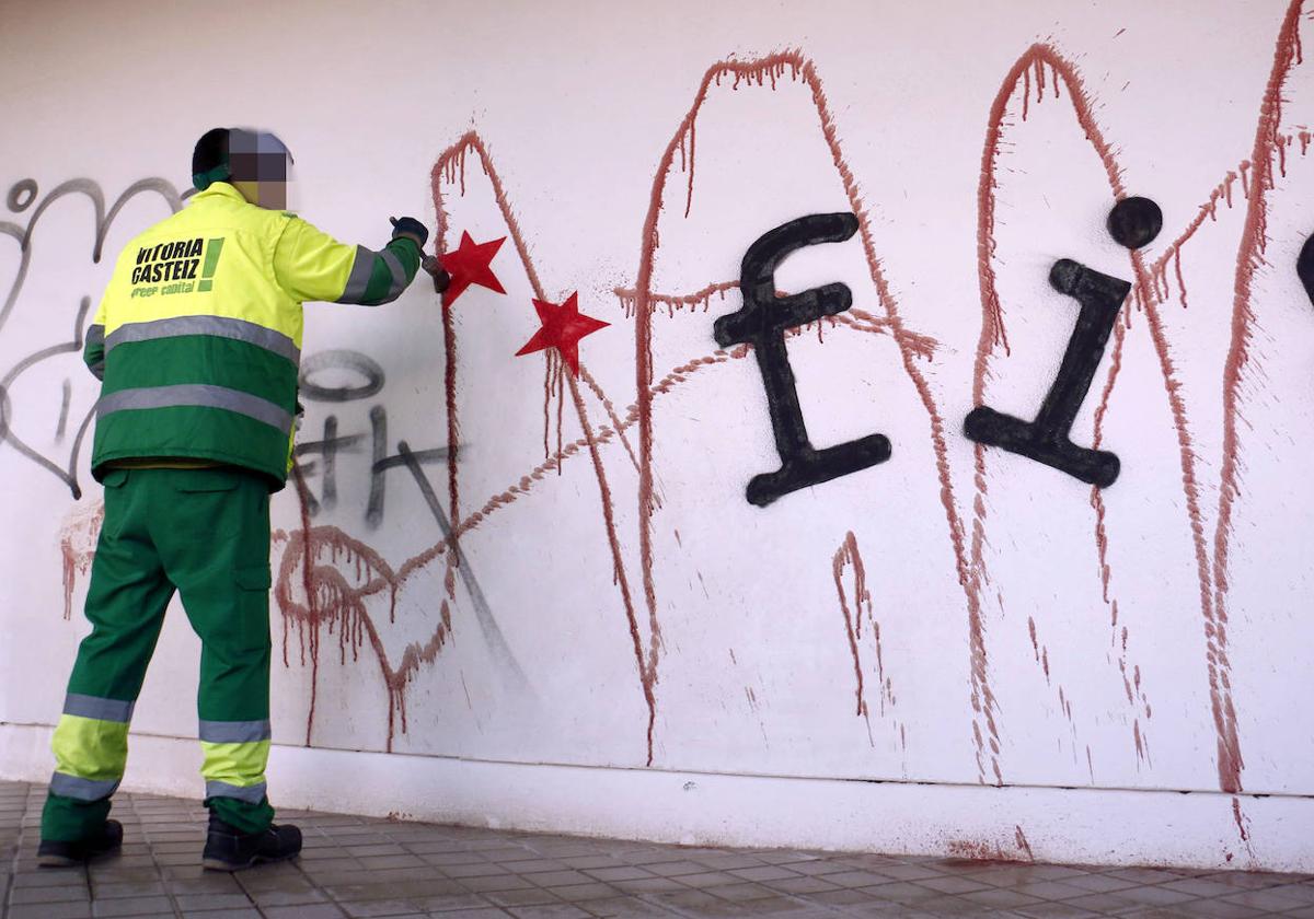 Un empleado municipal limpia una pintada antigua.