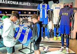 Dos jóvenes aficionados del Deportivo Alavés examinan las nuevas camisetas en la tienda del club.