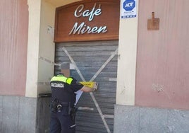 Un agente de la Policía Local colocando el precinto en la puerta de entrada al bar.