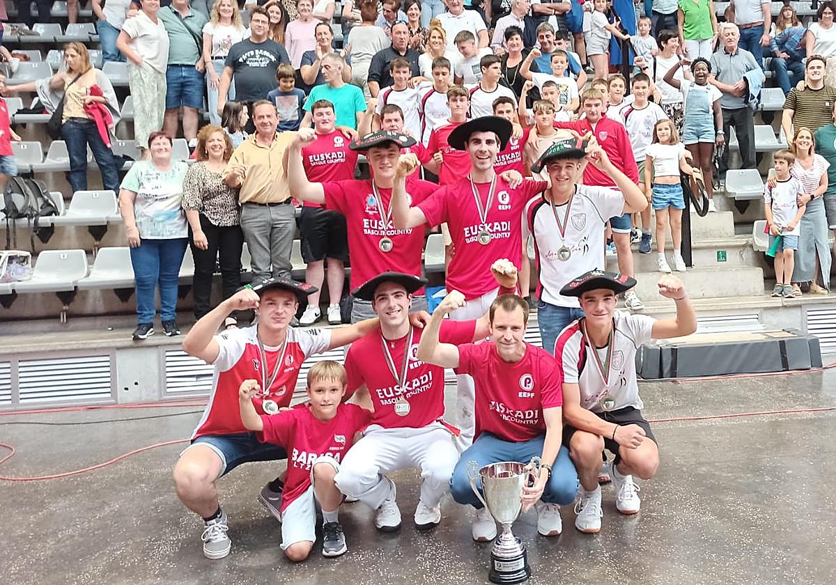 Los integrantes del club de pelota a mano de Markina con los trofeos y sus seguidores detrás.
