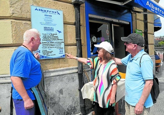 El camarero del Albatros atiende a dos turistas que revisan el menú del día.