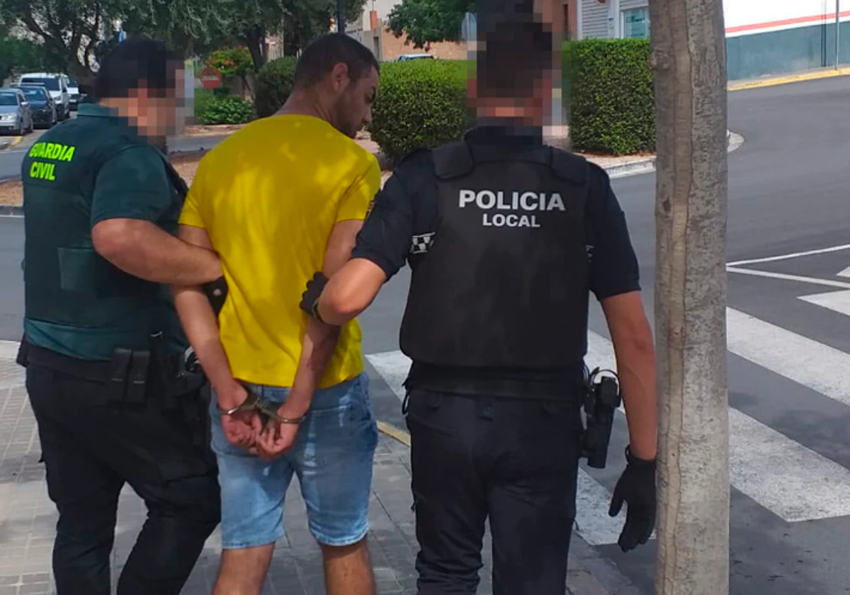 Un guardia civil y un policía trasladan al detenido a un coche patrulla.