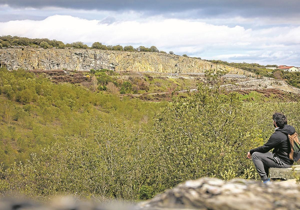 Un joven sentado observa el paisaje con la mina de Nanclares en el horizonte.