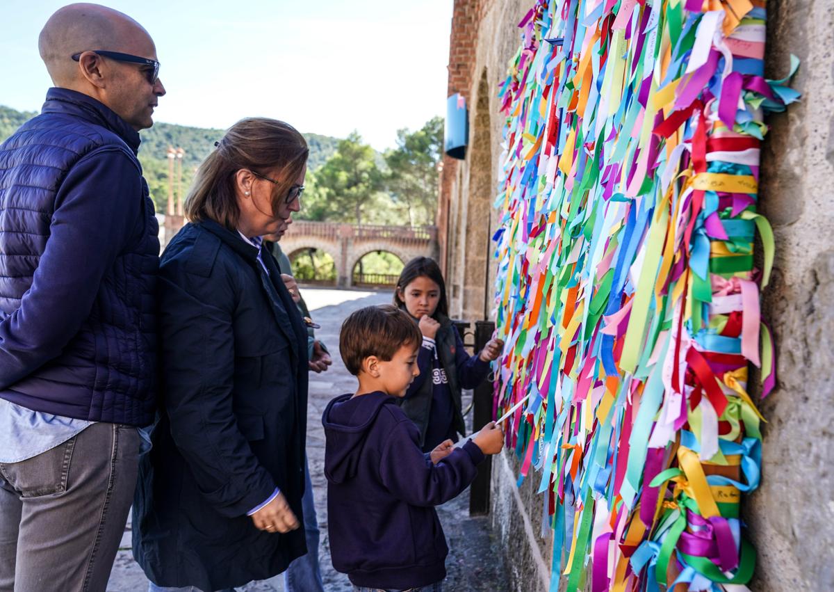 Imagen secundaria 1 - Un sacerdote reza en el santuario, frente al retablo y la escultura de Escrivá de Balaguer. Mariaje, Juan Pablo y dos de sus hijos, con las cintas para anudar. Mireia lee un folleto. 