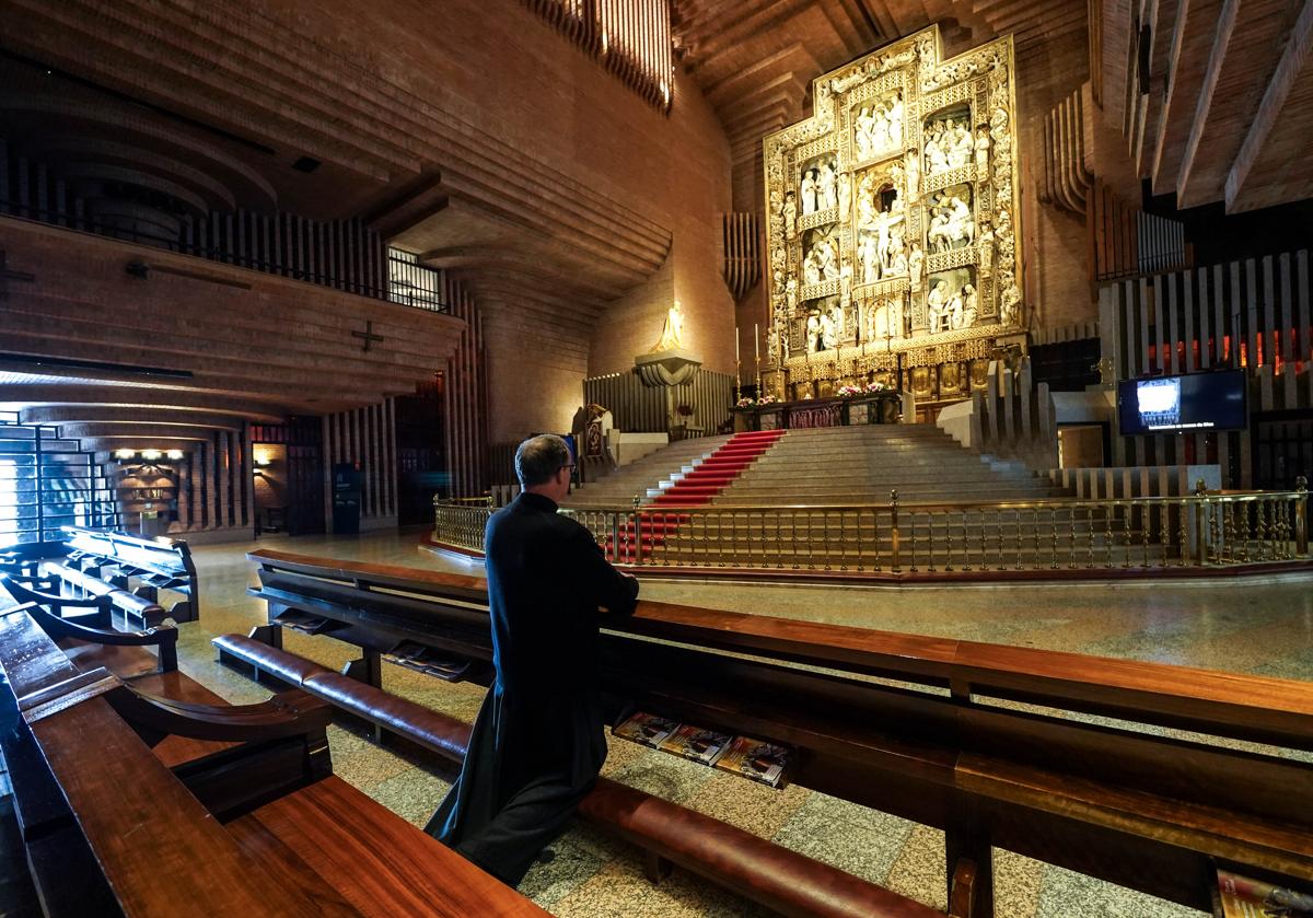 Imagen principal - Un sacerdote reza en el santuario, frente al retablo y la escultura de Escrivá de Balaguer. Mariaje, Juan Pablo y dos de sus hijos, con las cintas para anudar. Mireia lee un folleto. 