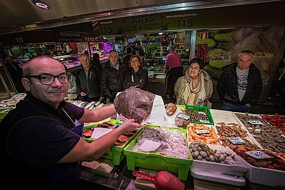 Un pescatero del mercado muestra un rodaballo ante la mirada de los clientes.