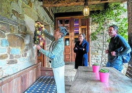 La propietaria de una casa rural recibe a dos de sus huéspedes mientras decora la entrada.