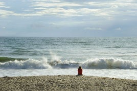 Una mujer sentada en la playa mira en soledad a las olas del mar