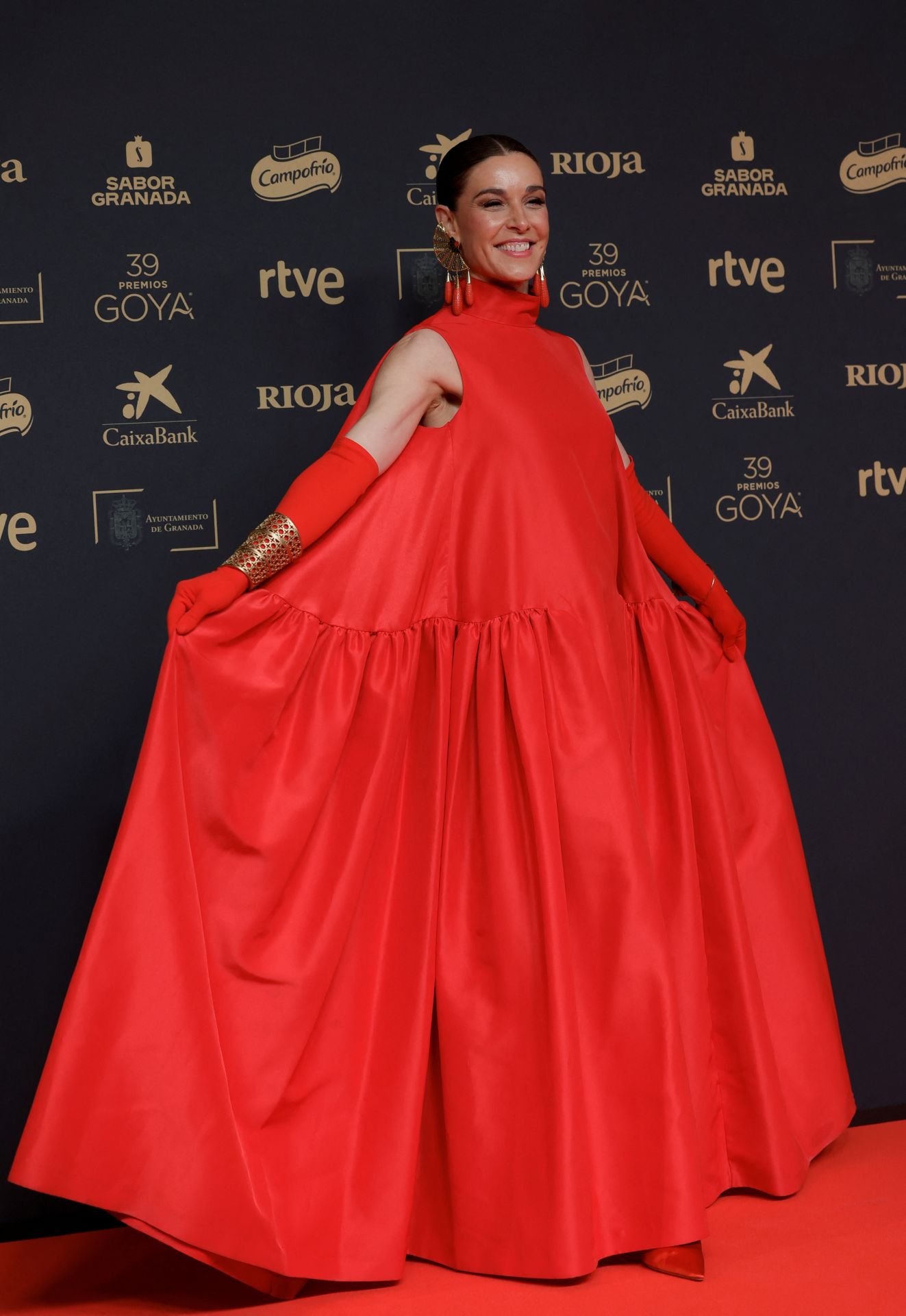 La presentadora Raquel Sánchez Silva ha optado por un vestido rojo muy original, inspiración Cristóbal Balenciaga y confeccionado en tafetán, que ha combinado con unos guantes del mismo tono y unos pendientes de gran tamaño que aportaban un aire aún más especial al look. Un diseño de Leandro Cano.