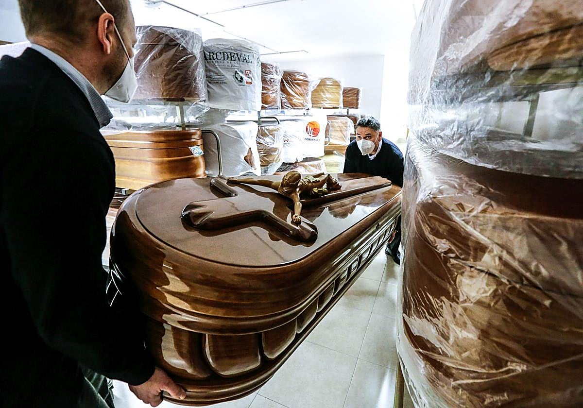 Dos empleados de una funeraria, completamente ajena a la información, transportan un féretro.