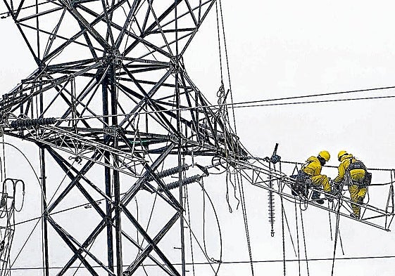 Varios operarios reparan una línea de alta tensión.