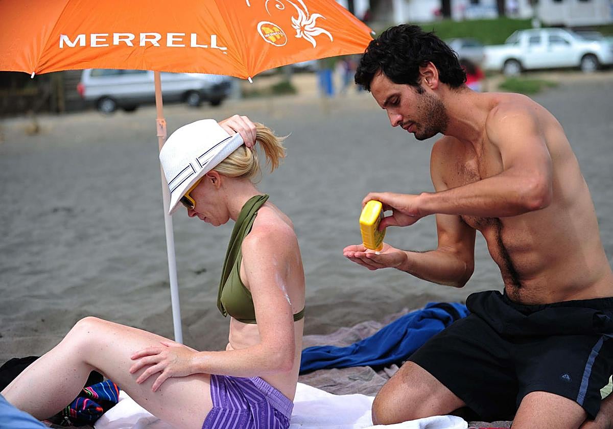 Un hombre aplica crema solar en la espalda de su pareja.