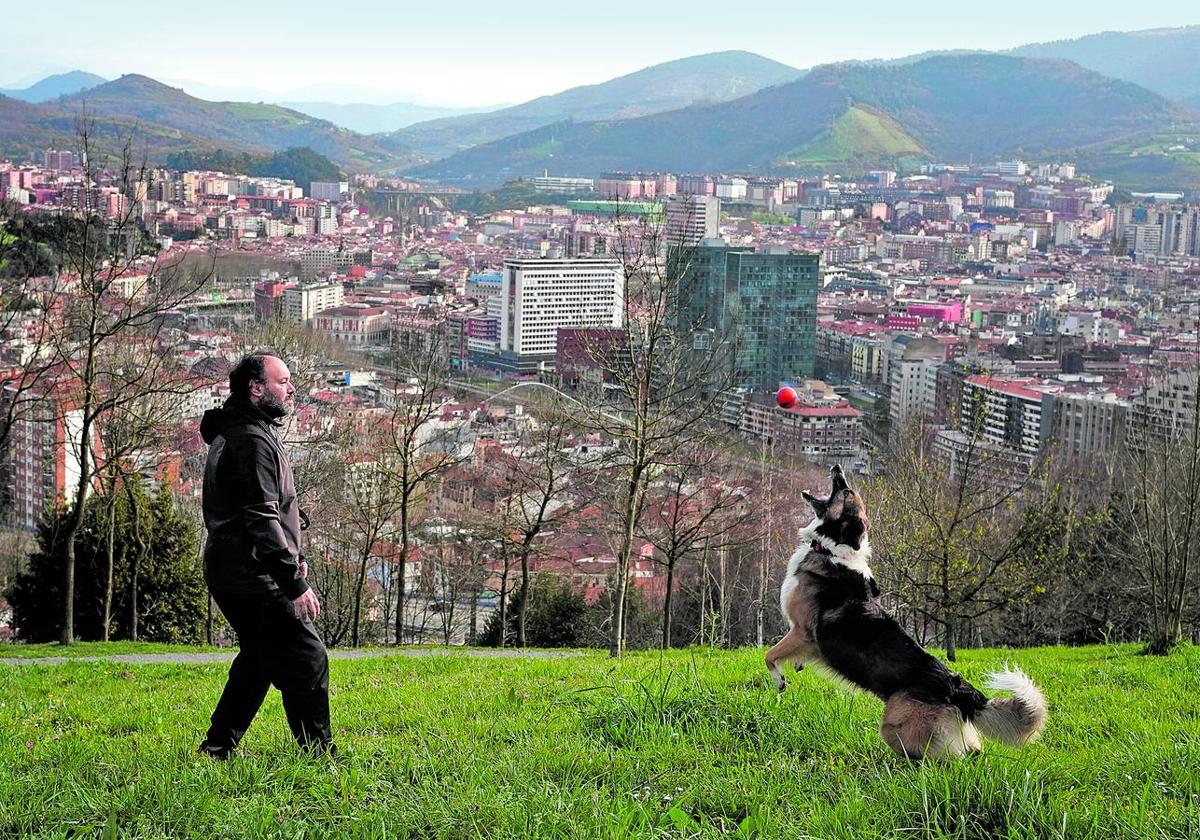 Miguel y su perro 'Klaus' juegan en las faldas del monte Artxanda, con el centro de Bilbao al fondo.
