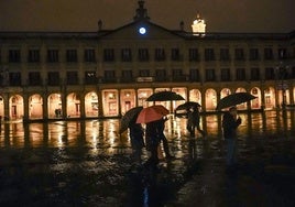 Los viandantes, con paraguas, pasean por una oscura plaza de España.