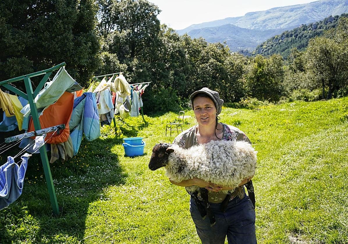 Imagen principal - Una residente con uno de los corderos de la ecoaldea. La francesa Silvie, de vuelta en su casa tras hacer compost con estiércol, junto a Ibon, estudiante pamplonés que está haciendo aquí prácticas de ganadería. El suizo Maiitrico y la valenciana Laura preparando la comida comunal.