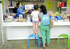 Dos lectoras atienden a las recomendaciones de la experta en una de las casetas de libros infantiles montadas en el Arenal bilbaíno.