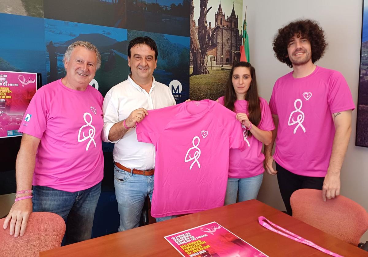 El alcalde, Eduardo Briones, presenta la marcha rosa con miembros de la Asociación Contra el Cáncer de Muskiz e Iván Miñambres, que ha diseñado la camiseta de este año.