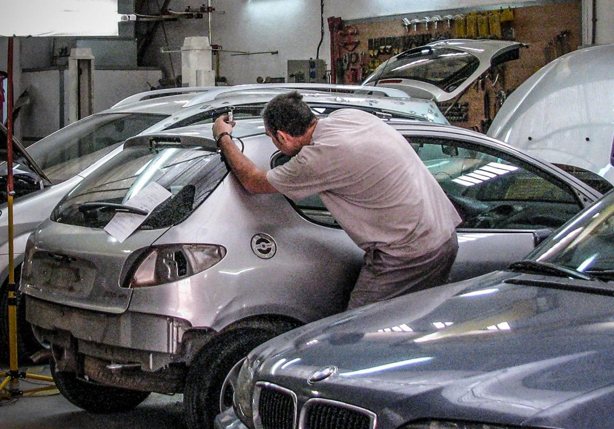 Un operario ajeno a la información repara la chapa de un vehículo en un taller.