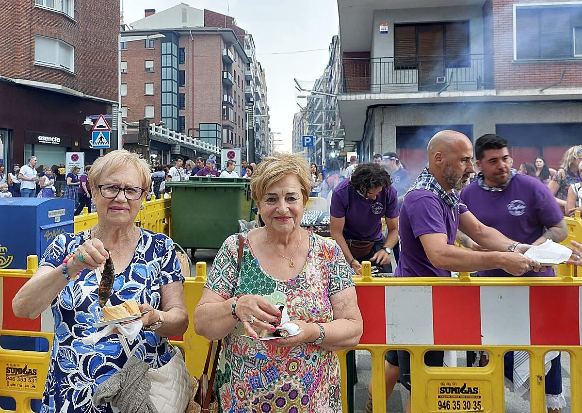 Imagen secundaria 1 - Las pailas abarrotaron las calles Itsasalde y Juan XXI. Abajo, Jina Zamarreño y Piedad Villacorta antes de degustar las sardinas.
