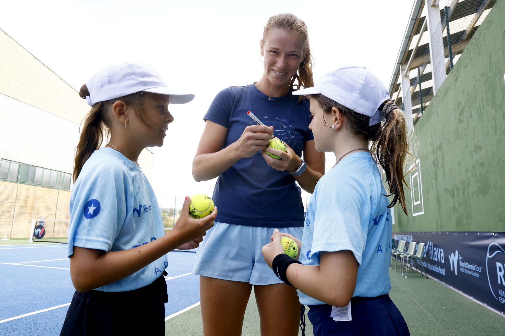 Jessika Pochet firma pelotas de tenis a dos jóvenes aficionadas.
