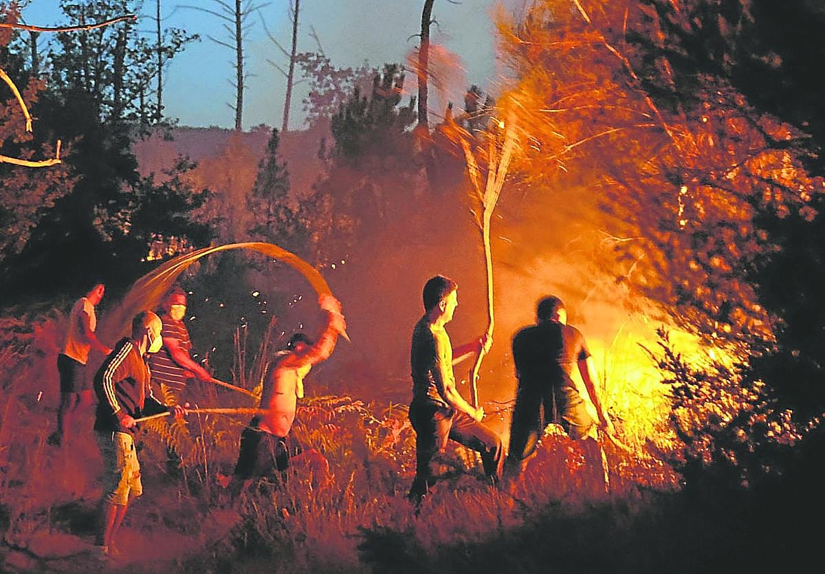 Unos vecinos intentan extinguir las llamas de un incendio forestal en Vilar de Condes, en la provincia de Ourense, en Galicia.