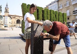 Dos personas se refrescan en la fuente de la plaza de la Virgen Blanca.