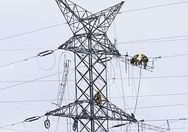 Dos operarios revisan una torre de alta tensión.