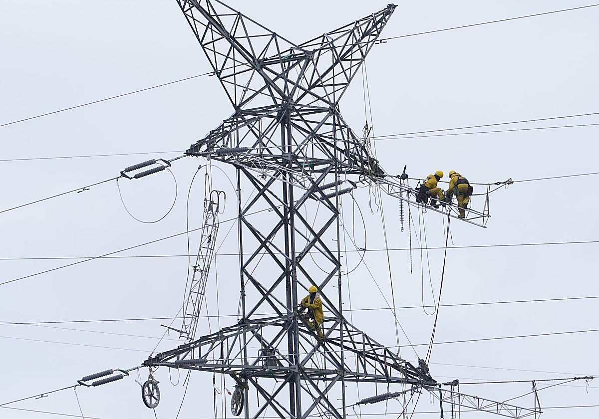 Dos operarios revisan una torre de alta tensión.