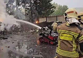 Dos profesionales y el robot tratan de apagar el fuego originado en un montón de chatarra.
