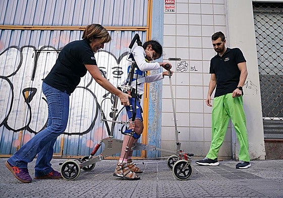 Ixone, con un exoesqueleto, camina por la calle con la ayuda de los fisioterapeutas de Pitxuflitos, especializados en pacientes con problemas neurológicos.
