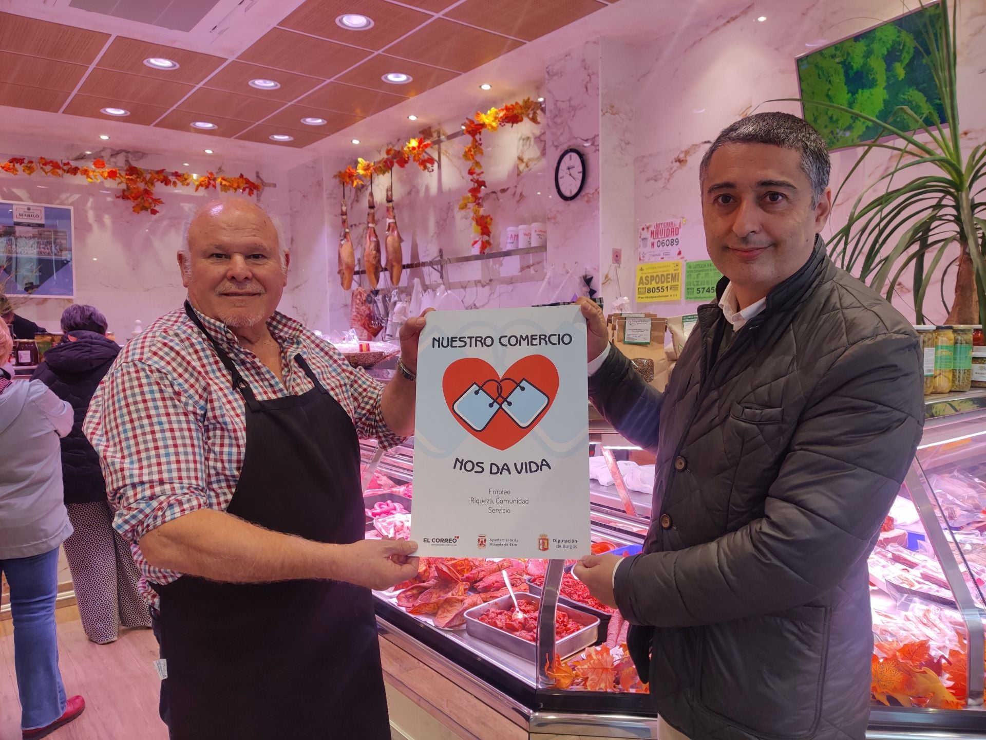 Imagen principal - Jorge Castro, el diputado provincial, con el responsable de Carnicería Mariló, Miguel Ángel Adrián, concejal de Promoción Económica, en Resines; y otro cartel más con corazón en Amelia Complementos.