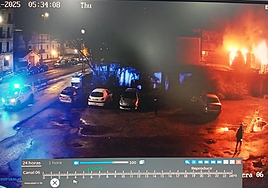 Una cámara de seguridad capta la llegada de la Ertzaintza, a las 4.34 horas, aunque el reloj marca las 5.34. A la derecha de la imagen, el vecino de la caseta de al lado observa la dimensión de las llamas.