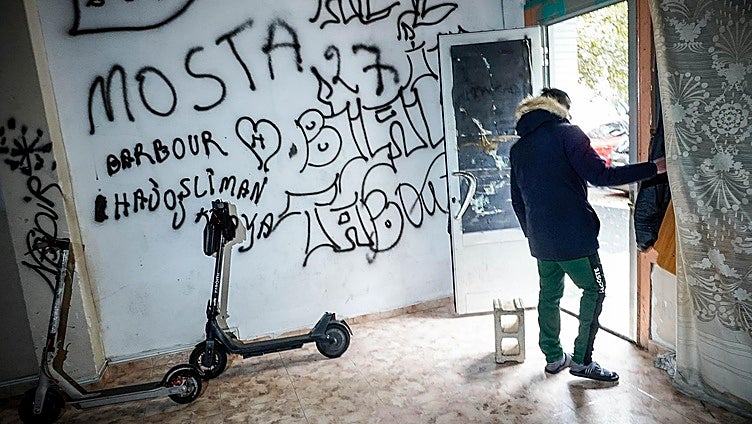 Dos patinetes en una lonja okupada de Coronación. En la puerta, un joven que declara «buscar trabajo» y que en su país era «marinero».