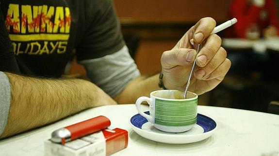 Un hombre fuma un cigarrillo en una cafetería antes de la ley antitabaco.